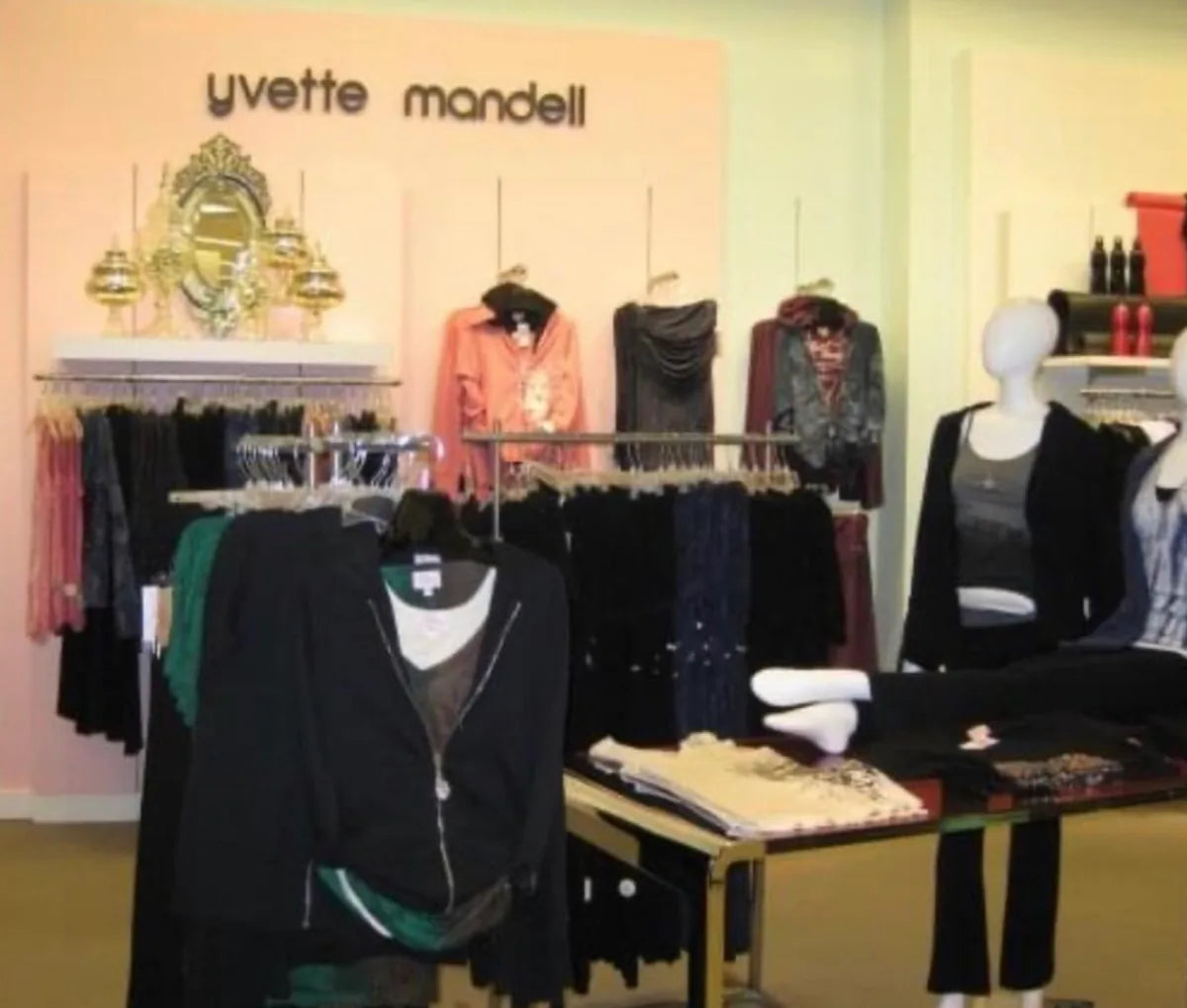 An in-store Yvette Mandell shop within a department store, the name mounted above racks of jeweled knits and a gilt mirror