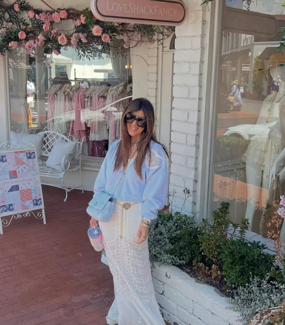 Yvette outside a LoveShackFancy storefront, wearing the powder-blue crystal bow hoodie with a white lace skirt